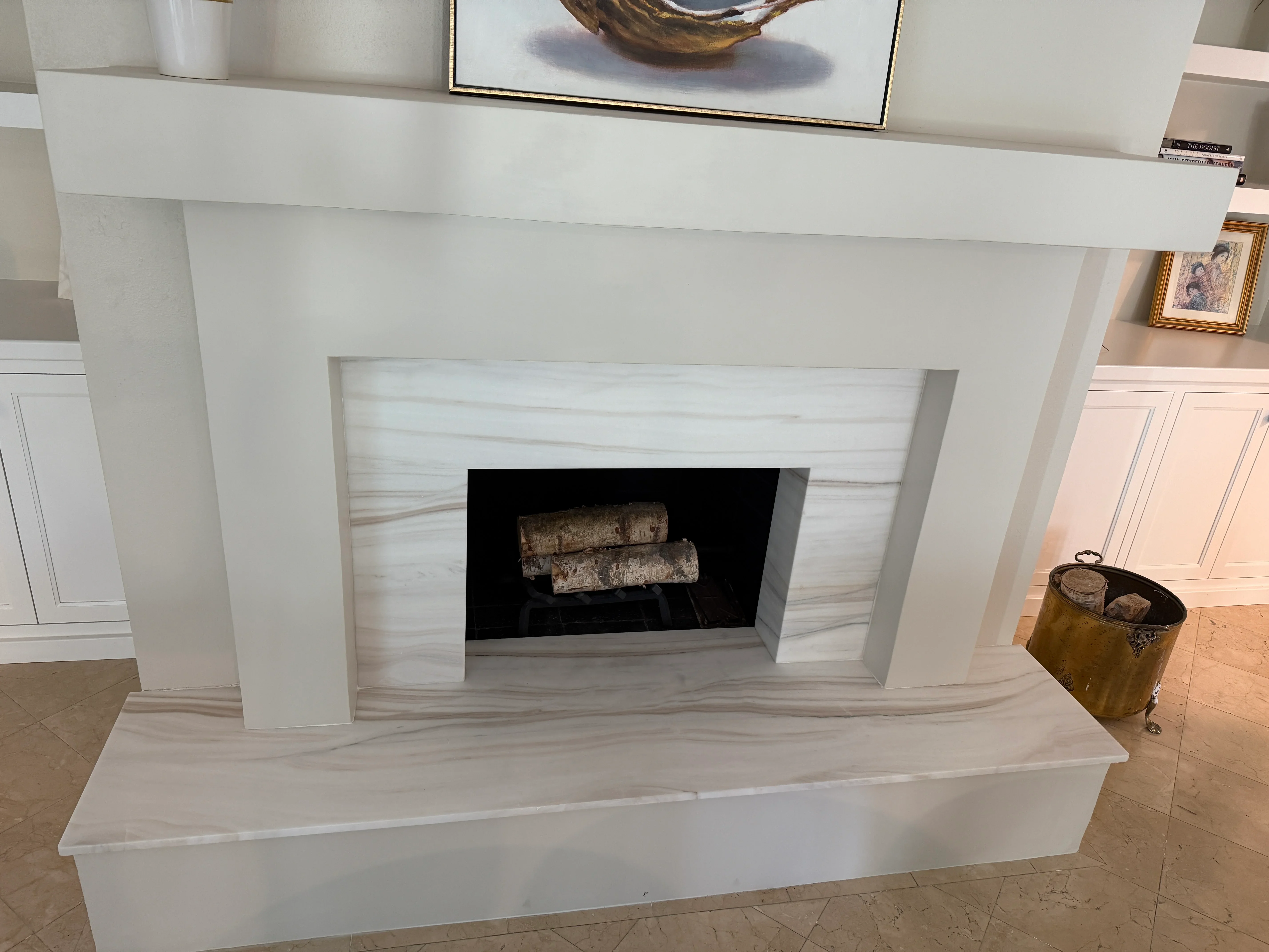 Modern fireplace with light marble surround, black firebox, and decorative logs