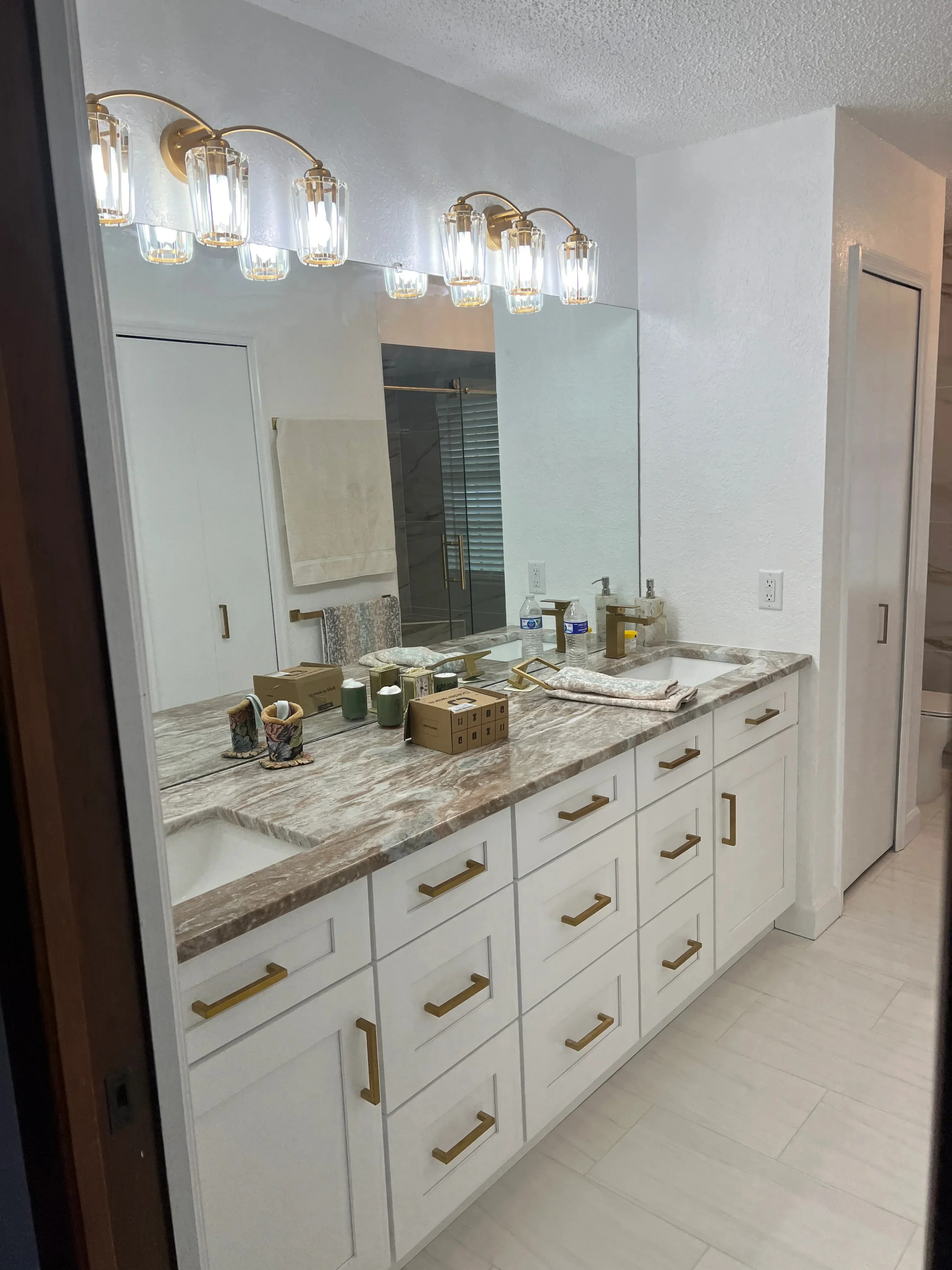 Modern bathroom vanity with white cabinets, marble countertop, brass fixtures, and contemporary lighting