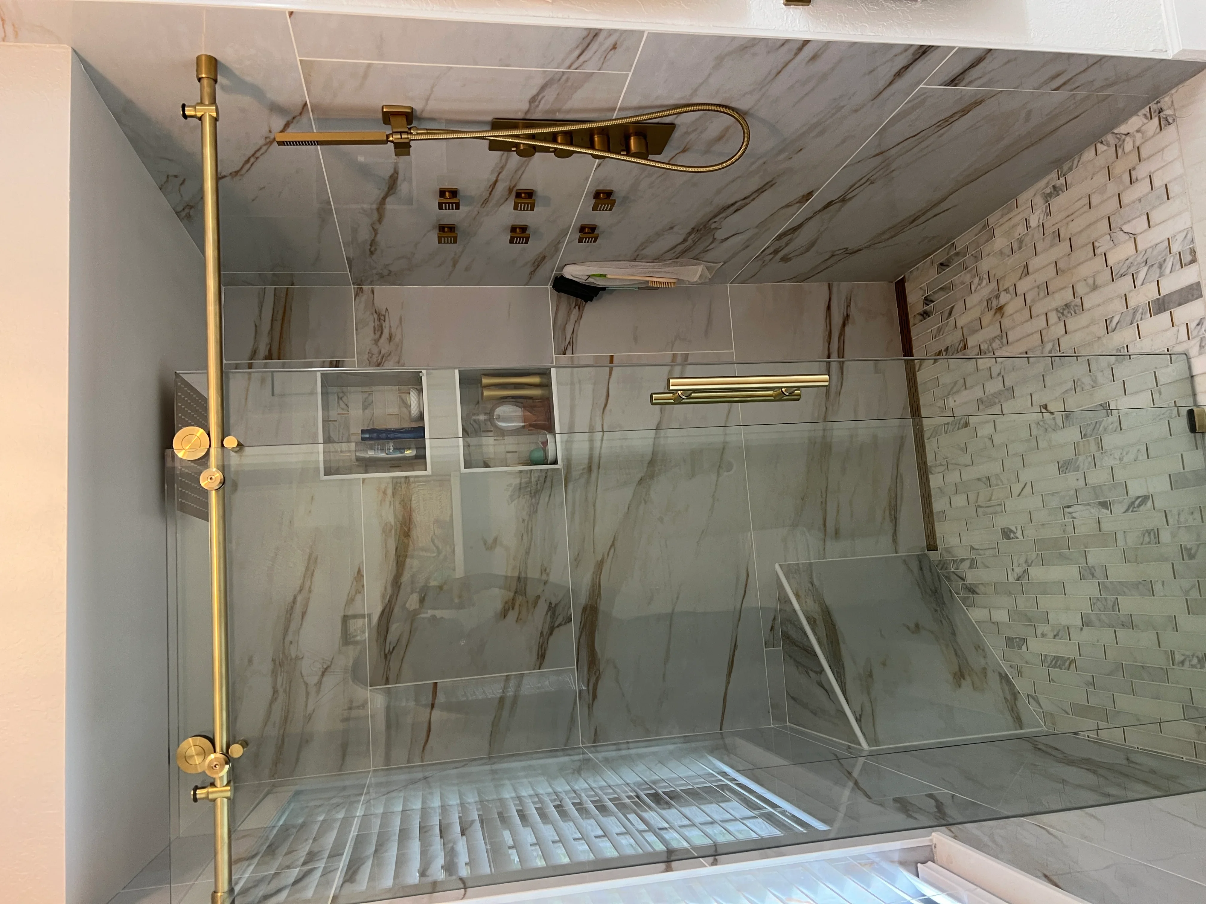 Luxury shower with marble tile, frameless glass enclosure, and brass fixtures