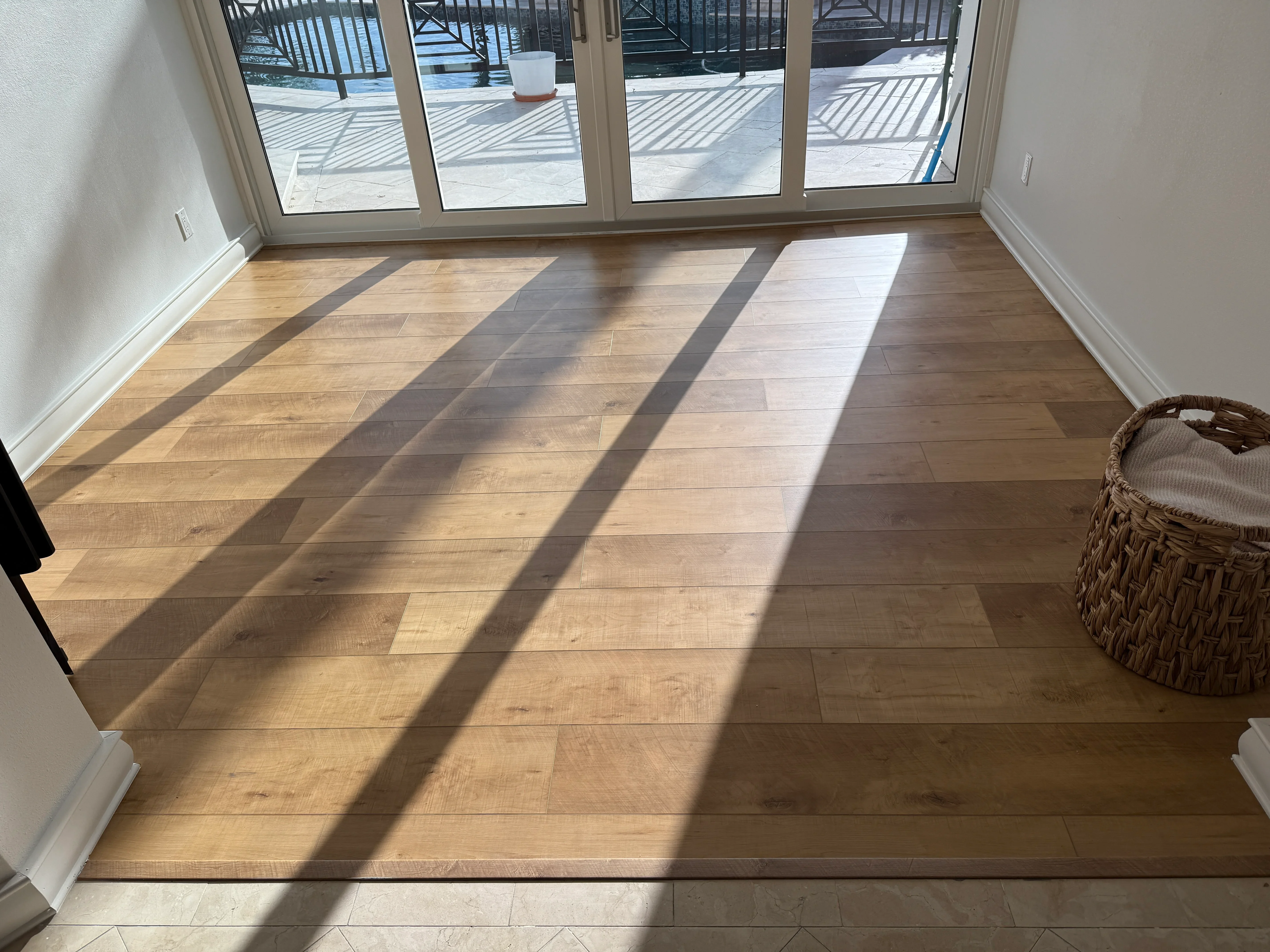 Newly installed hardwood flooring in sunlit room with glass doors overlooking deck