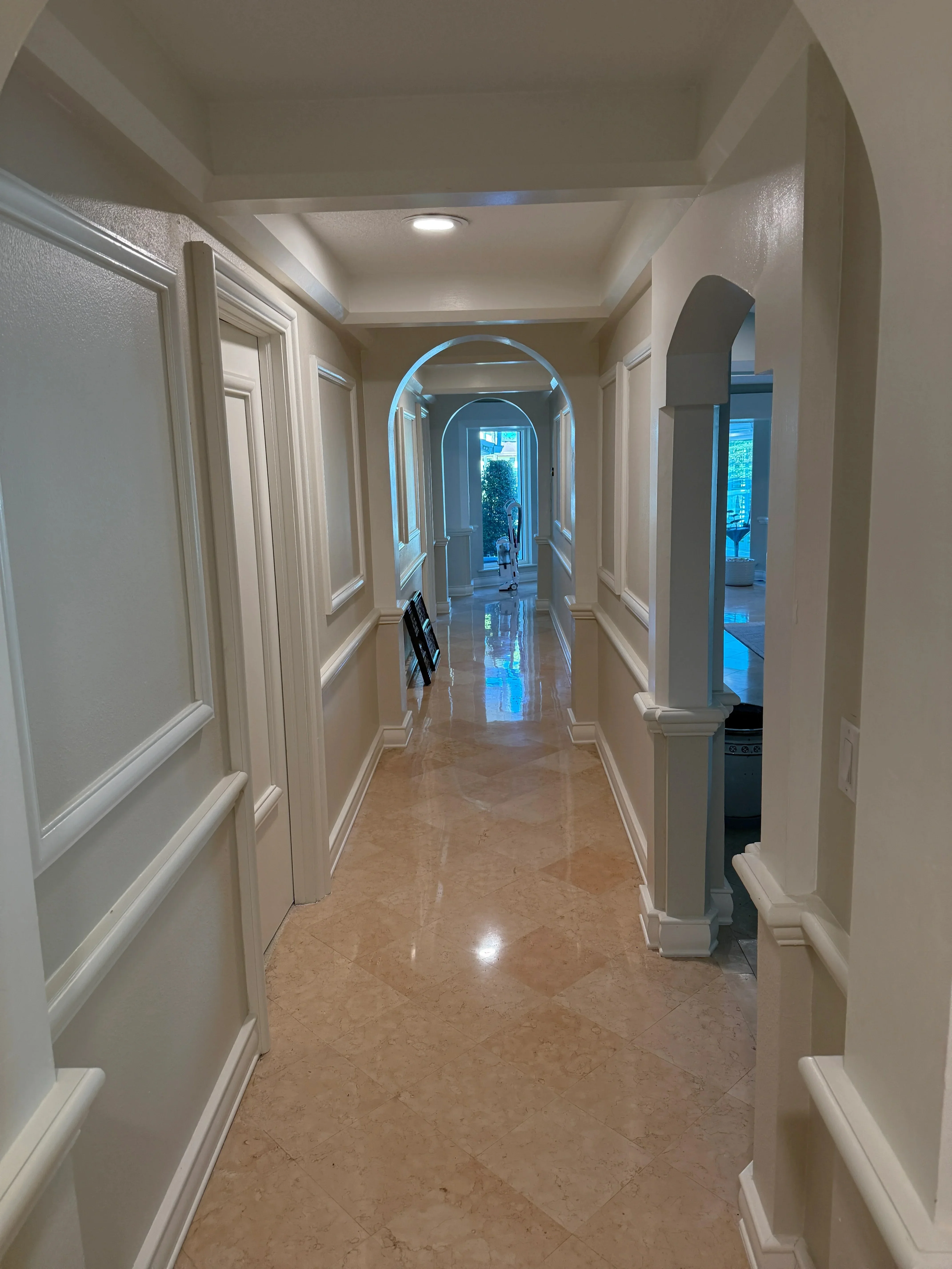 Bright hallway with white panel doors, travertine flooring, and arched doorways with columns
