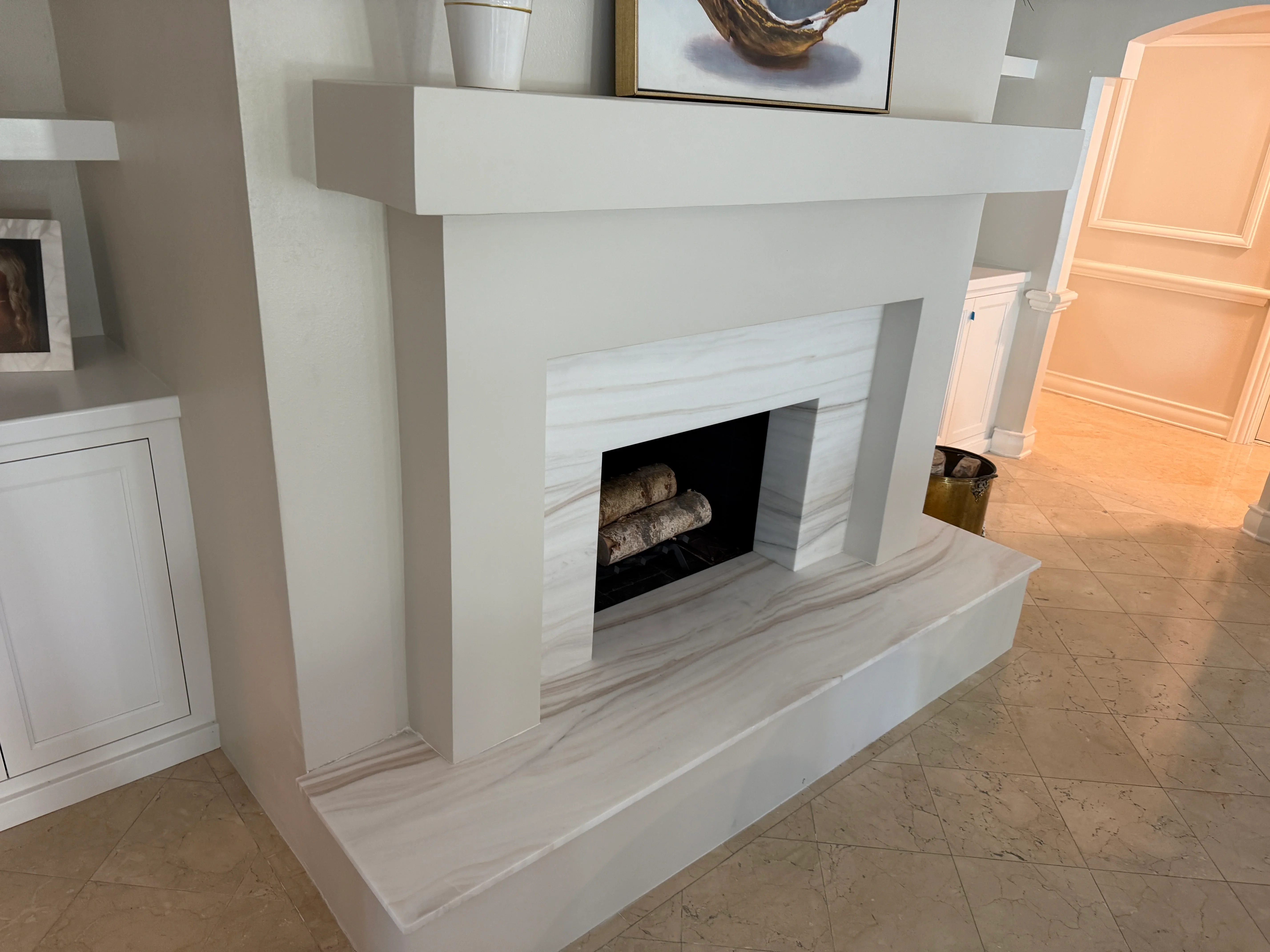 Modern fireplace with white and gray marble surround, black firebox, and decorative logs