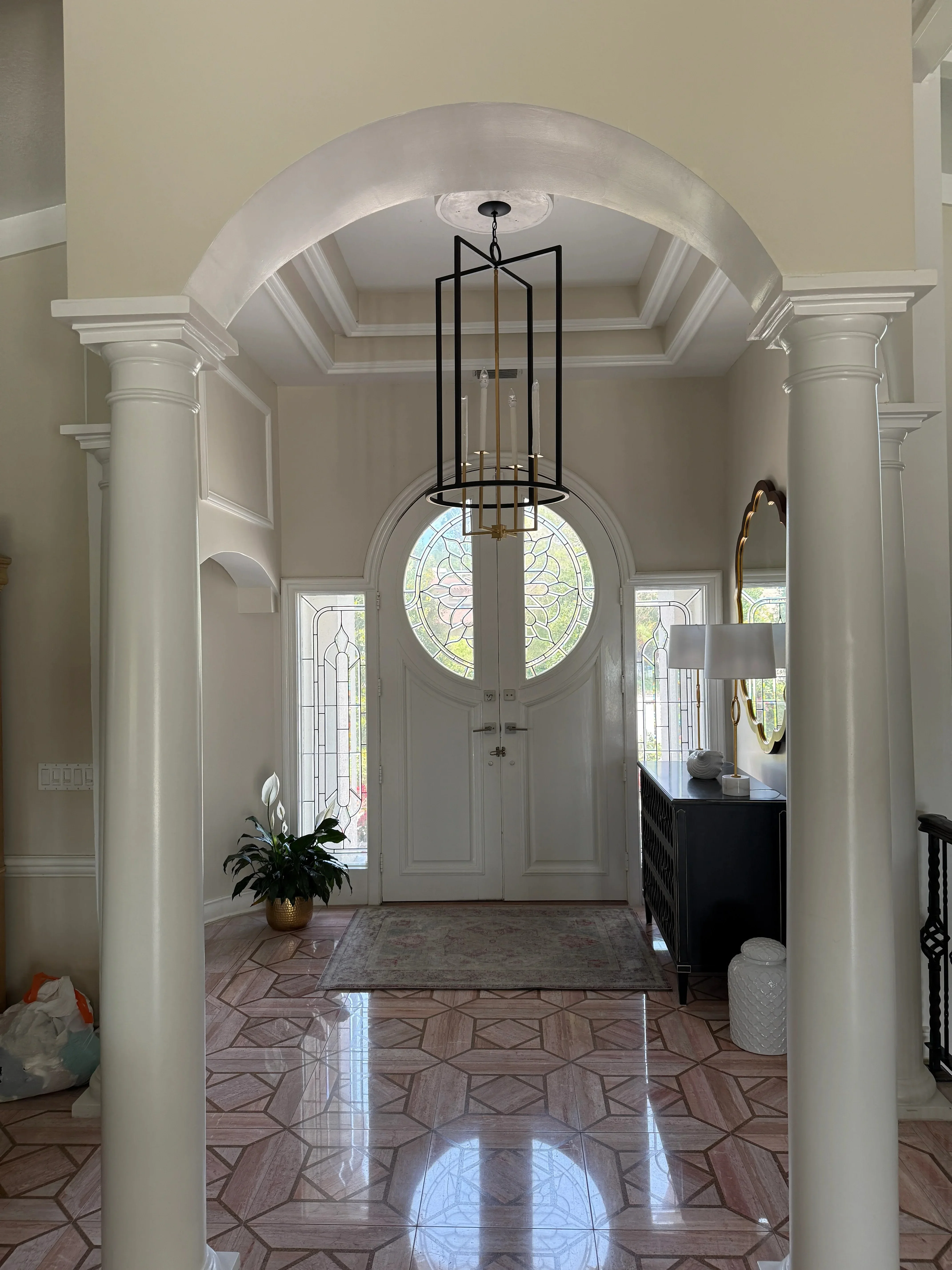 Elegant foyer with barrel vault archway, white columns, geometric wood floors, and stained glass window
