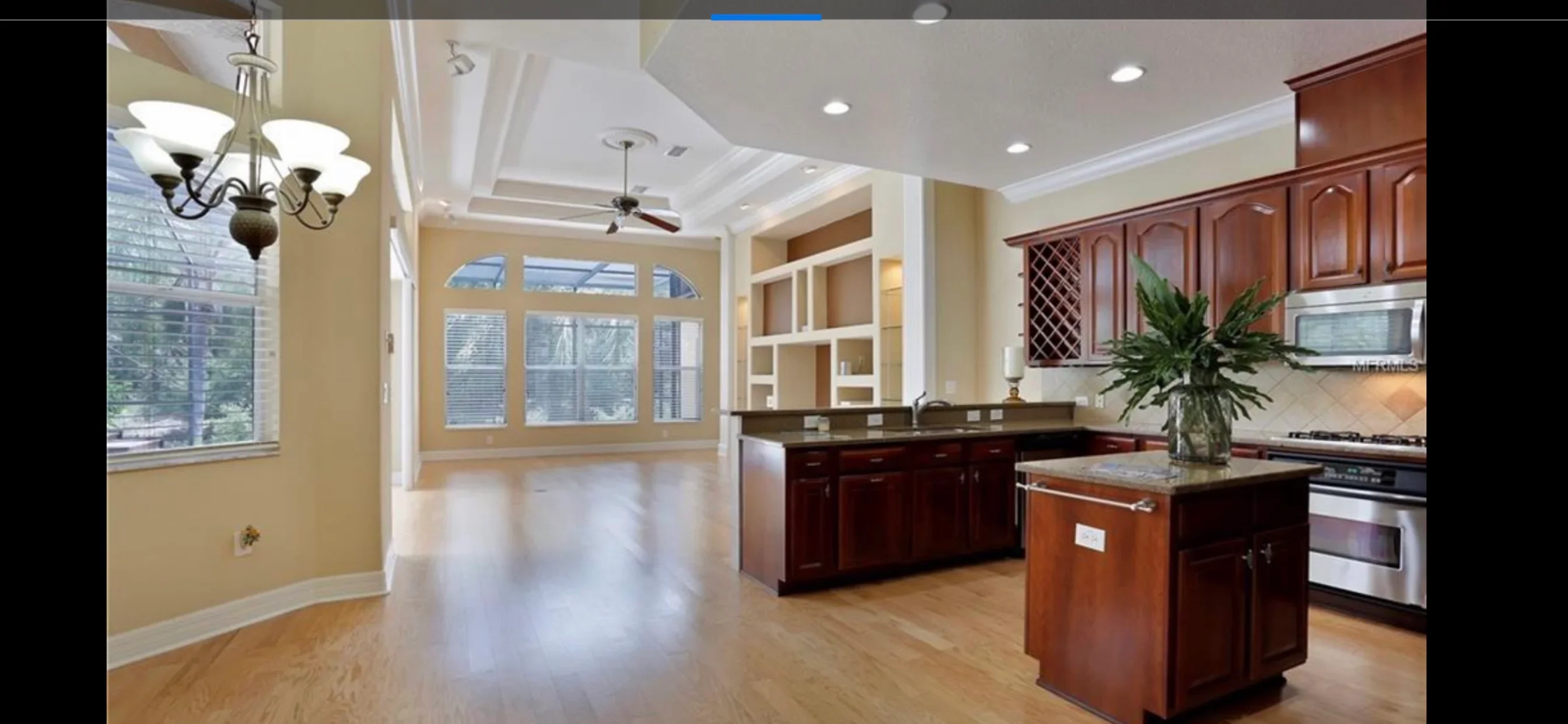 Modern kitchen with cherry cabinets, island, and open living area with coffered ceiling