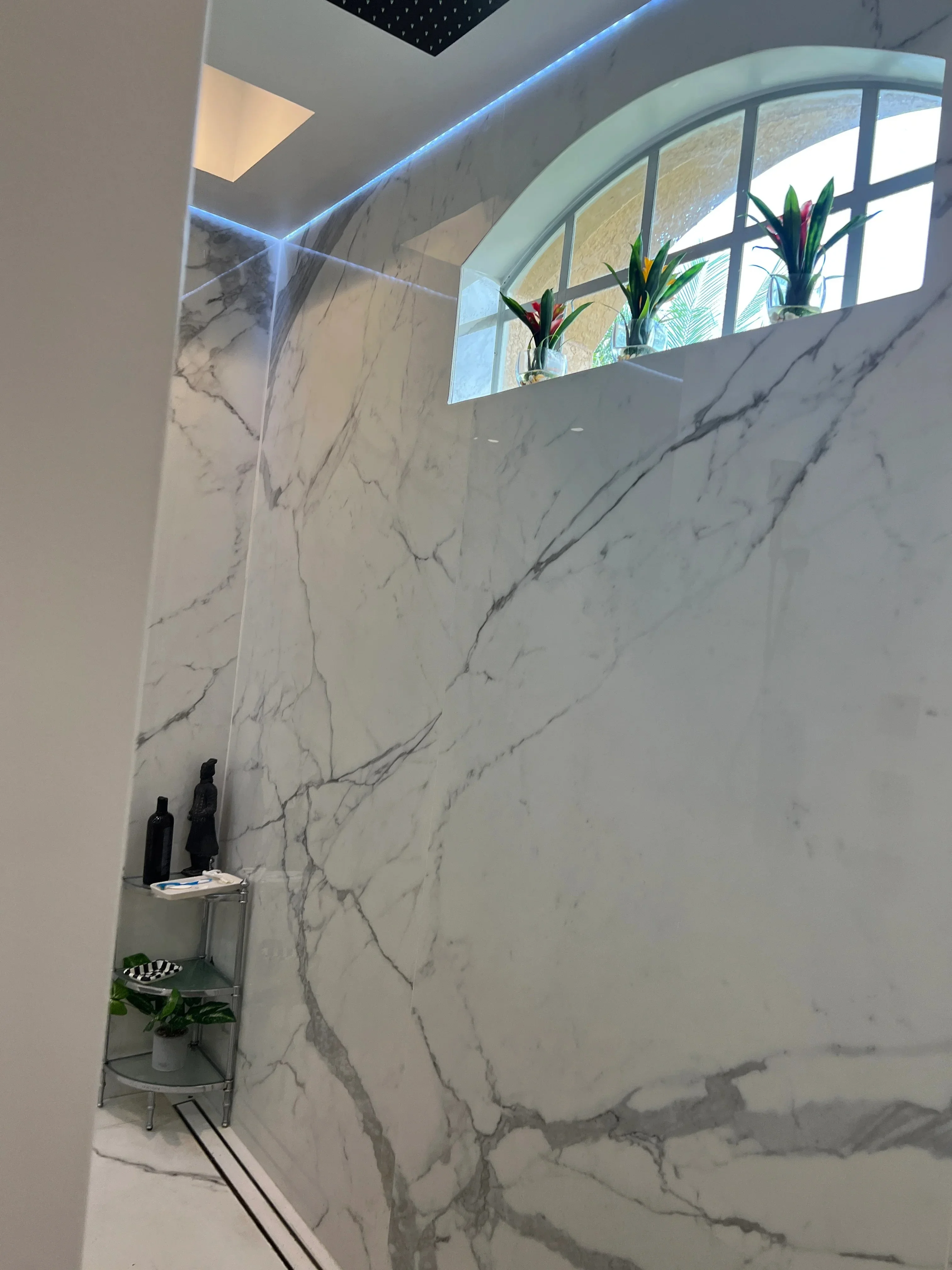 Modern bathroom with marble walls, arched window, and blue ceiling accent lighting