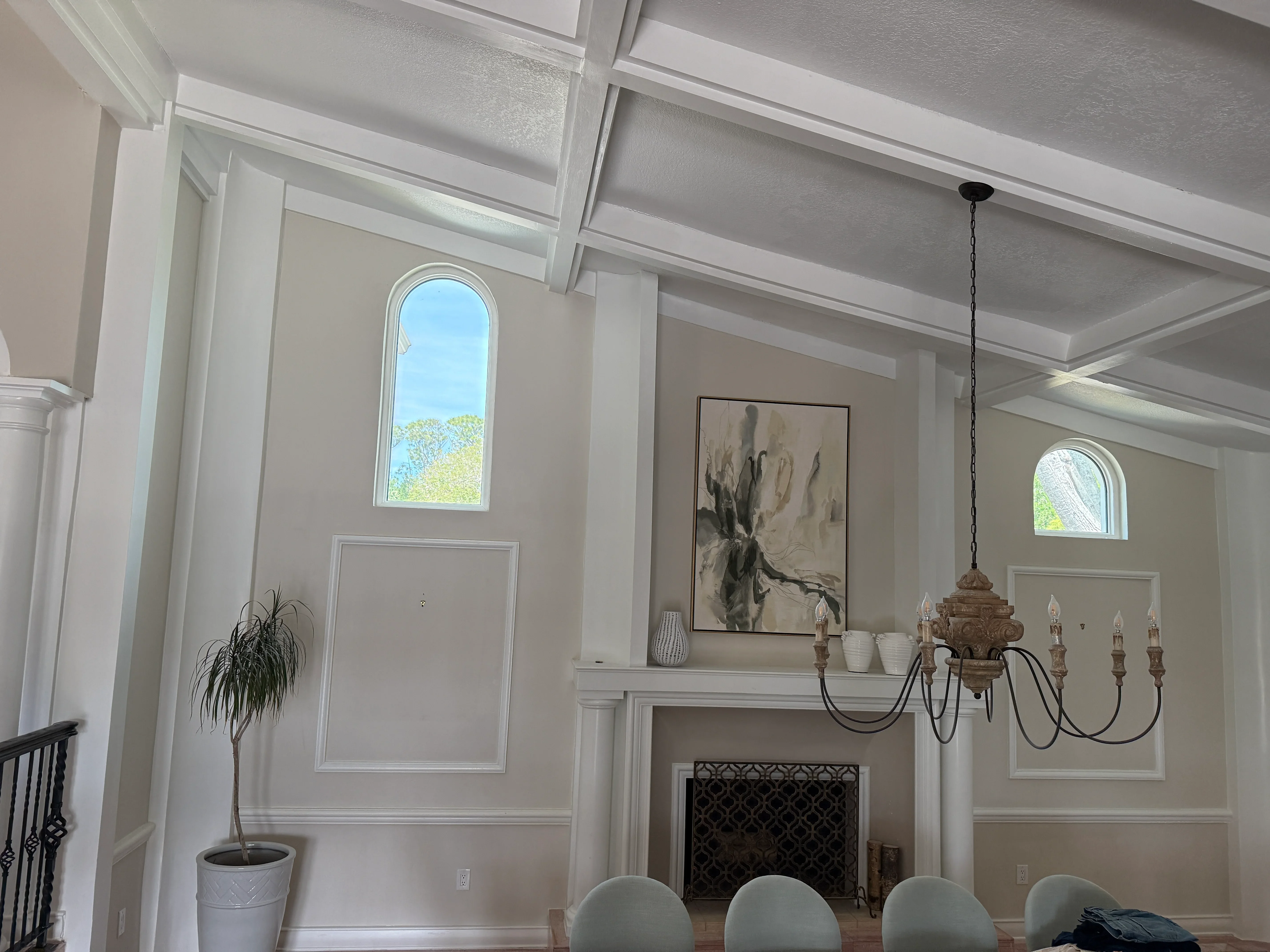 Bright great room with white coffered ceiling, fireplace surround, and arched windows