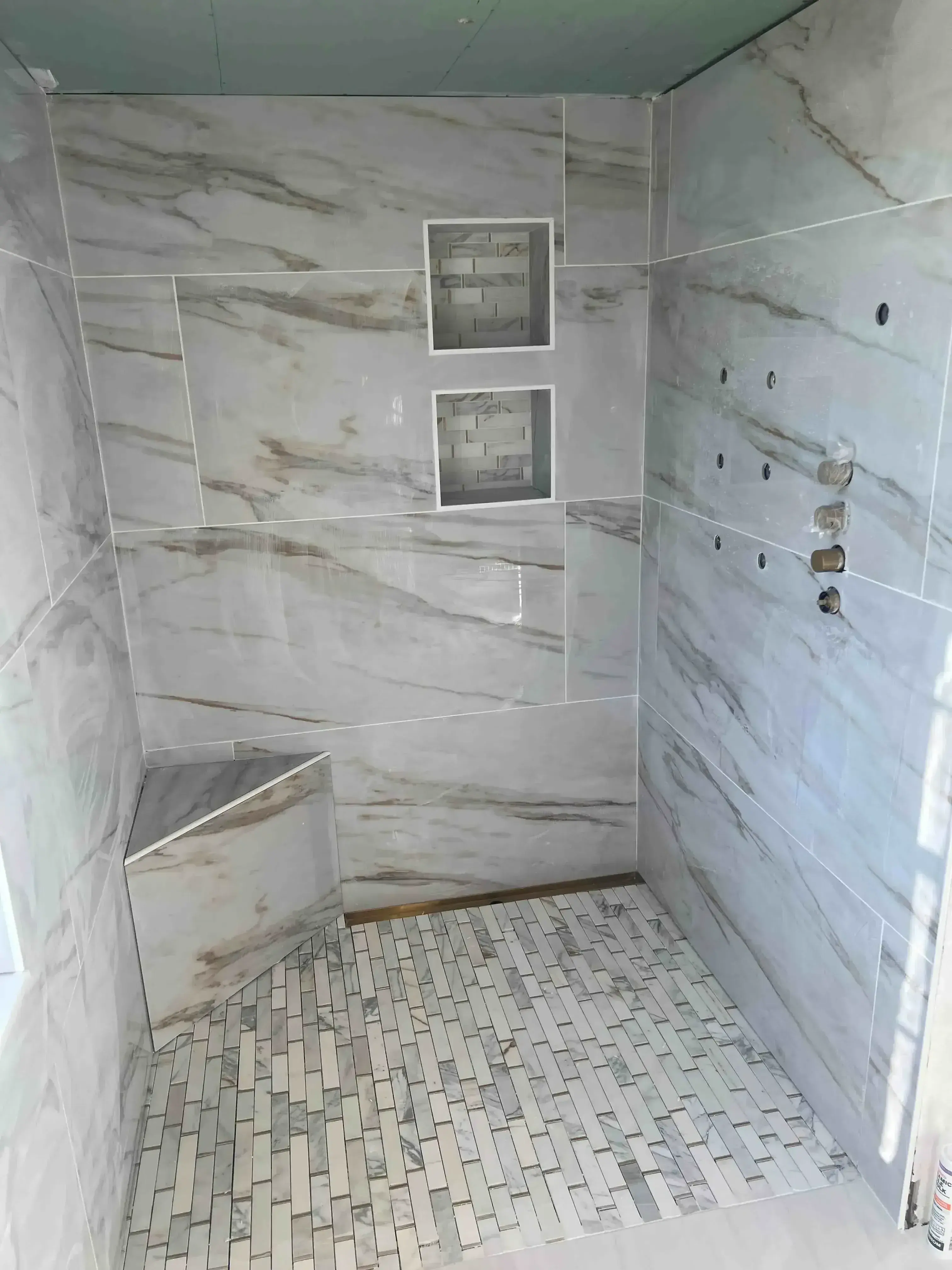 Luxury bathroom shower with marble-look tile walls, ceiling, and subway tile accent wall